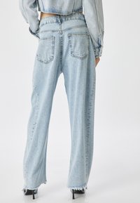 Jeans de tiro alto en azul claro con un corte relajado, dobladillos deshilachados y dos bolsillos traseros. Hechos de denim con una textura ligeramente desvanecida.