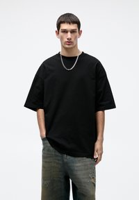 Tricou oversized negru din bumbac, cu mâneci scurte și decolteu rotund, asortat cu blugi ușor distruși, de culoare albastru deschis.