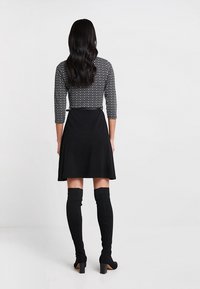 Robe noire avec une jupe évasée, haut à manches trois-quarts à pois, associé à des chaussettes noires montantes et des talons.