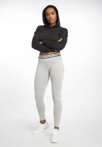 Zwarte cropped hoodie met een koord en grijze leggings met een zwarte tailleband en witte tekstdetails, gedragen met witte sportschoenen.