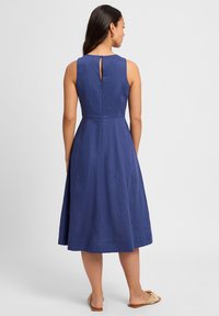 Mouwloze blauwe jurk met een aansluitend lijfje en een uitlopende rok. Heeft een keyhole achterkant met een knoopsluiting en een gladde textuur.