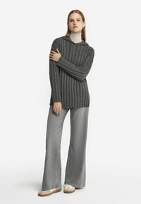 Szary prążkowany sweter z kapturem, z długimi rękawami i luźnym krojem, zestawiony z szerokimi szarymi dżinsami i jasnokolorowymi sneakersami.