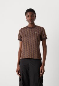 Braun gemustertes T-Shirt mit geometrischem Design, kurzen Ärmeln, Rundhalsausschnitt und kontrastierendem Besatz, kombiniert mit schwarzen Cargo-Hosen.