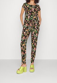 Floral outfit featuring a black top and matching pants with vibrant pink and green patterns; paired with chunky lime green platform sandals.