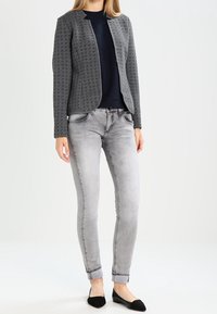 Szary, teksturowany żakiet na ciemnej bluzce, zestawiony z jasnoszarymi, obcisłymi dżinsami. Czarne baleriny dopełniają stylizację. Prosty i dopasowany krój.
