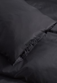 Ropa de cama de tela negra con una superficie suave, que cuenta con un borde fruncido en una almohada y una sección plana de la manta.