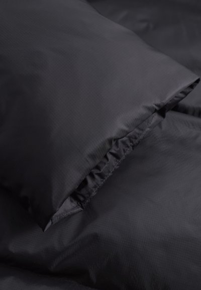 Bedding en tissu noir avec une texture lisse, présentant un bord froncé sur un oreiller et une section plate de la couverture.