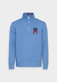 Blå halvmatchad sweatshirt i bomullsblandning, med ribbad krage och ärmslut, samt broderad logotyp i röd och marinblå. Slät textur.
