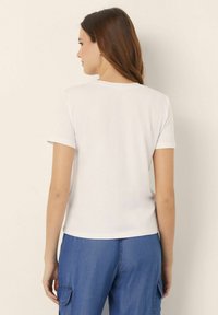 Tricou alb cu mânecă scurtă din bumbac, cu guler rotund și o croială lejeră, purtat cu pantaloni cargo din denim albastru. Design simplu.