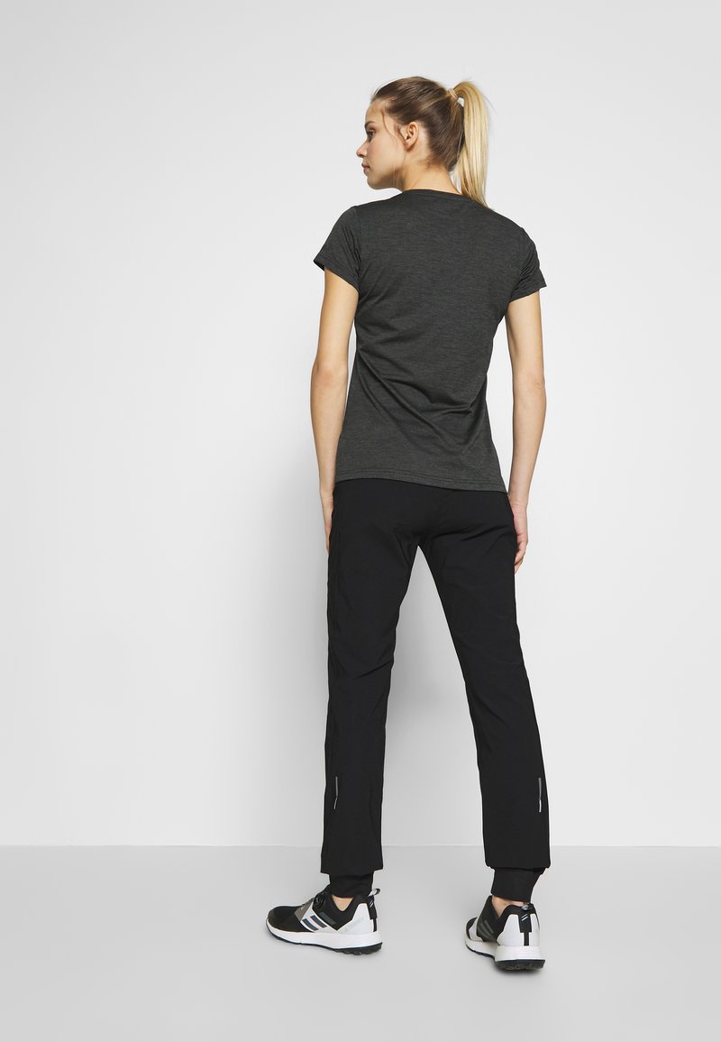 Graues Kurzarm-T-Shirt, schwarze schmal geschnittene Hose mit Reißverschlüssen an den Saumenden und schwarz-weiße Sportschuhe. Glatter Stoff, minimalistisches Design.