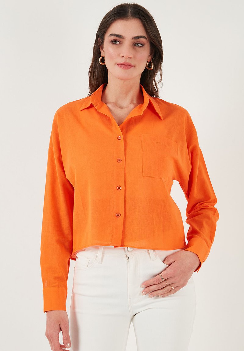 Orange, cropped button-up shirt with a collar, long sleeves, and a chest pocket; made of lightweight fabric with a smooth texture.
