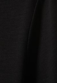 Čierna tkanina s hladkou, rovnomernou textúrou. Makro záber ukazuje mäkký, ľahký materiál s jemným leskom a minimálnymi švíkovými detailmi.