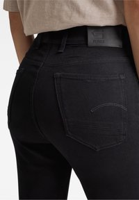 Jeans de mezclilla negra con bolsillos traseros, con una textura suave y un logotipo sutil en un parche de cuero en la cinturilla.
