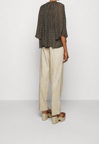 Pohodlná blůza s krátkým rukávem černé barvy se vzorem; doplněná o světle béžové volné kalhoty; platformové sandály s tkanými detaily.