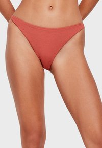 Slip di bikini rosso a coste con un design a vita bassa e copertura minimale, con bordi lisci e un tessuto testurizzato.