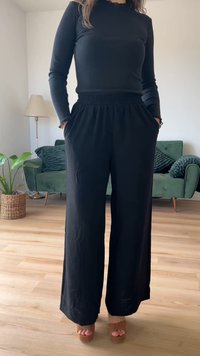 Calças largas pretas feitas de tecido suave, com uma cintura alta e bolsos. Combinadas com uma blusa preta de mangas longas e sapatos plataforma castanhos.