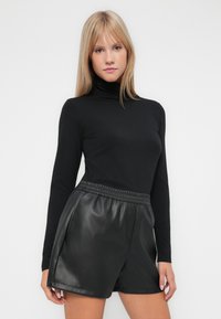 Zwart langemouwen top met een aansluitende col, gecombineerd met zwarte neplederen shorts met een elastische tailleband en zijzakken.