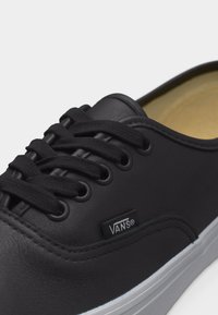 Μαύρο αθλητικό παπούτσι Vans χαμηλού ύψους με μαύρα κορδόνια, μαύρες τρύπες κορδονιών και λευκή λαστιχένια σόλα σε κοντινή λήψη.