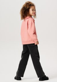 Rosa sweatshirt med en volangkrage, kombinerad med svarta vida jeans och kraftiga svarta skor. Slät textur, avslappnad passform, inga synliga mönster.