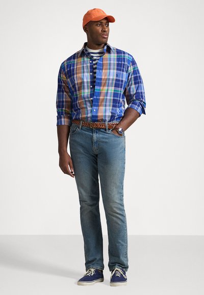 Blå og brun rutete skjorte over en stripete t-skjorte, sammen med blå jeans, oransje caps og blå sko. Har et flettet brunt belte og klokke.