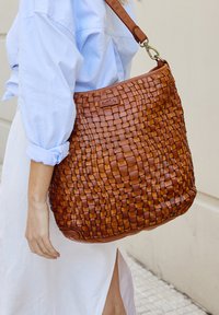 Borsa a tracolla in pelle intrecciata di un ricco marrone con una finitura testurizzata, dotata di una tracolla resistente e di un logo discreto sul davanti.