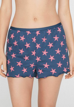 Marineblaue Shorts mit pinkem Seesternmuster, getragen von einer Person, die vom Bauch bis zur Mitte des Oberschenkels gezeigt wird, Hände entspannt an den Seiten.