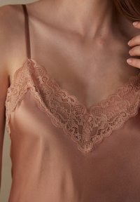 Camisón de satén en un cálido tono malva con delicados bordes de encaje en el escote, finas tirantes ajustables y una textura suave.