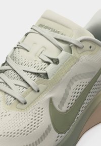 Κοντινό πλάνο του αθλητικού παπουτσιού Nike Pegasus 42 σε μπεζ και ανοιχτό πράσινο χρώμα, που αναδεικνύει τα κορδόνια, το πλεκτό επάνω μέρος και το λογότυπο Swoosh στο πλάι.