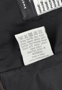 Black fabric label with care instructions and product details, including "Bodo Rain Jacket JR" and "Made in China." Text in clear font.
