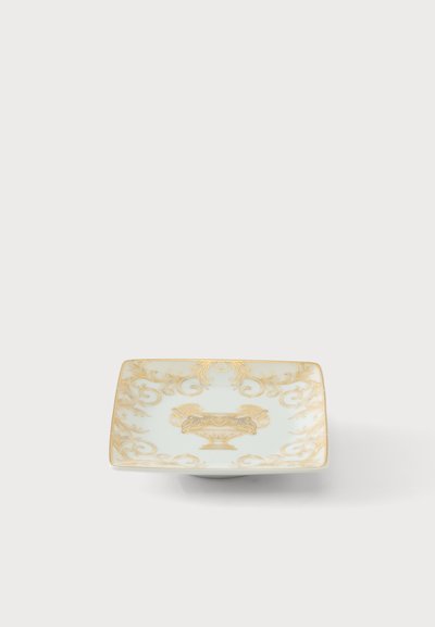 Assiette carrée en porcelaine blanche avec un décor floral et urne doré orné sur le bord et le centre, sur un fond clair uni.