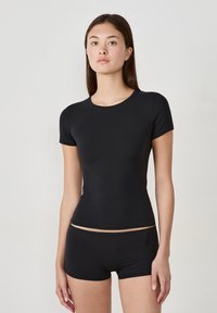 Cropped top nero a maniche corte, aderente e realizzato in un tessuto liscio, con scollatura rotonda, abbinato a pantaloni corti a vita alta in un materiale simile.