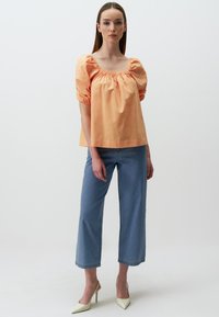 Blouse en coton pêche avec des manches bouffantes et un décolleté carré, associée à un jean cropped bleu clair et des escarpins beiges à bout pointu.