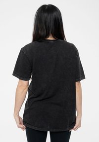 Black cotton t-shirt with short sleeves, relaxed fit, faded texture, and a rounded hem. Features visible stitching along the edges.