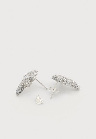 Ασημένια σκουλαρίκια καρφάκια με υφή που λαμπυρίζει και κυρτό σχήμα, με διάφανο πίσω μέρος για ασφαλή εφαρμογή.