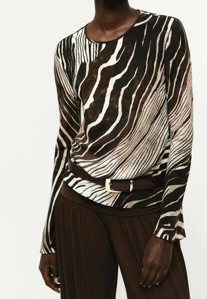 Haut à manches longues imprimé zèbre rentré dans un pantalon large marron foncé avec une ceinture marron foncé ornée d'une boucle dorée.