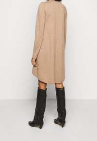 Robe tricotée marron clair avec des manches longues, un ourlet arrondi et une coupe décontractée, accompagnée de bottes en cuir noires jusqu'aux genoux.