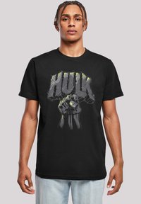 Tricou negru cu un design grafic al unei reintegrări a unei pumn și cuvântul "HULK" scris cu litere îndrăznețe și stilizate. Materialul pare moale și lejer.