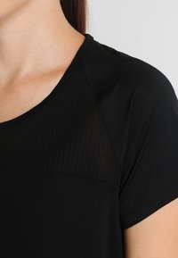 Svart idrottströja med korta ärmar, med en texturerad panel vid bröstet. Tillverkad av lätt, ventilerande tyg.