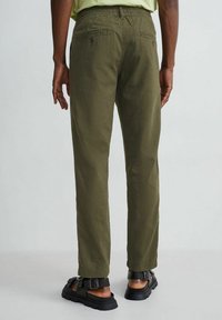 Spodnie bawełniane o prostym kroju w kolorze oliwkowej zieleni. Posiadają dwie tylne kieszenie i elastyczny pas. Noszone z czarnymi sandałami.