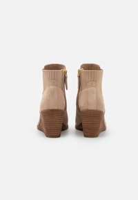 Bottines beiges à tige textile côtelée, en suède, avec un talon en bois. Elles arborent des zippers dorés et un branding subtil.
