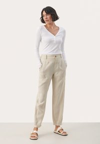 White long-sleeve henley top with a V-neck and buttons; light beige linen trousers with side pockets, cuffed hems, and a relaxed fit.