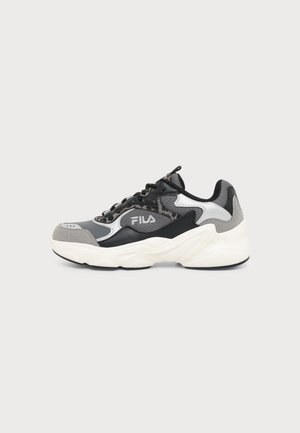 Šedý, čierny a biely FILA sneaker s hrubou bielou podrážkou a zvrškom z rôznych materiálov, zobrazený z vonkajšej strany na jednokolorovom pozadí.