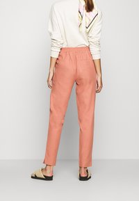 Světlé růžové zúžené kalhoty s elastickým pasem, texturovanou látkou a jednou zadní kapsou. V kombinaci s neutrálními plochými sandály a krémovým topem.