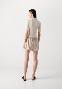 Gai beige ribota adīta blūze ar īsām piedurknēm, apvienota ar brīvi pieguļošām gaišām bežām šortiem. Modele valkā tumšas sandales un viņai ir garas taisnas mati.