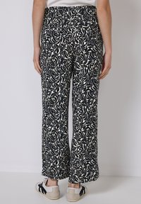 Wijde broek met een zwart en crèmekleurig bladmuster, gemaakt van lichtgewicht stof, met een hoge taille en zijzakken.