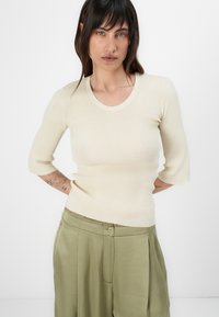 Ribbed beige short-sleeve top with a round neck, paired with olive green high-waisted trousers featuring a button closure and pleated details.