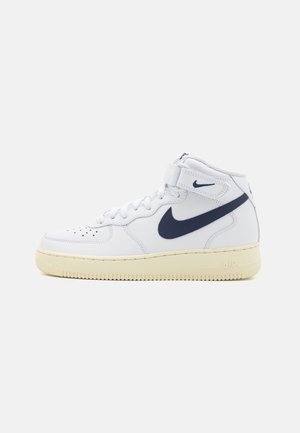 Bílé vysoké tenisky Nike Air Force 1 s tmavě modrým swoosh a suchým zipem, béžová podrážka a perforovaná špička.