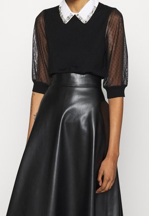 Pull noir avec des manches bouffantes transparentes, col blanc orné de strass. Jupe en cuir noir brillant avec une forme évasée.