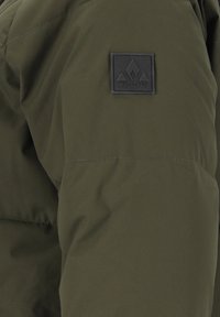 Oliven grøn pufferjakke har en glat tekstur med et syet design, et kvadratisk sort logo-patch på skulderen og en afslappet pasform.