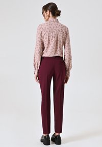 Blouse in lichtroze met bloemenprint, lange mouwen; gecombineerd met bordeaux rode pantalon, gedragen met zwarte plateau schoenen.